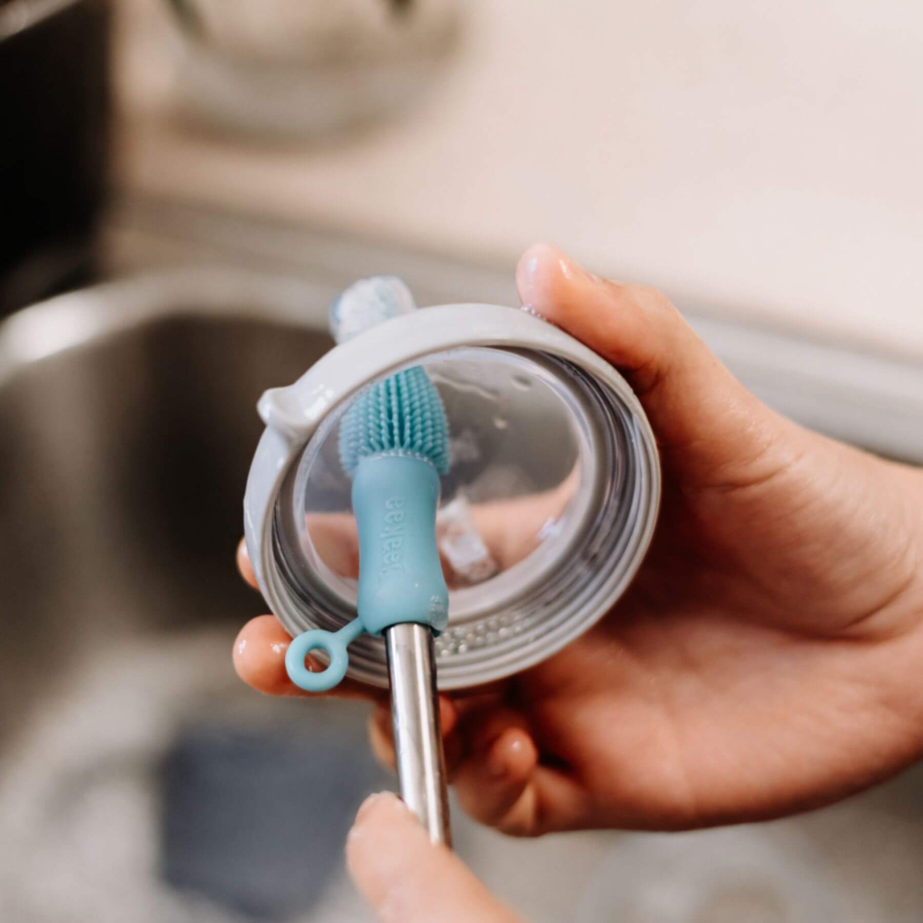 Person holding a cleaning brush with a blue bristle head and white handle over a container lid.