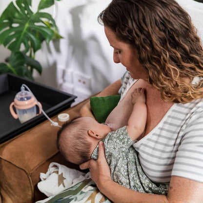 A woman breastfeeding a baby while sitting on a brown leather couch in a home setting.