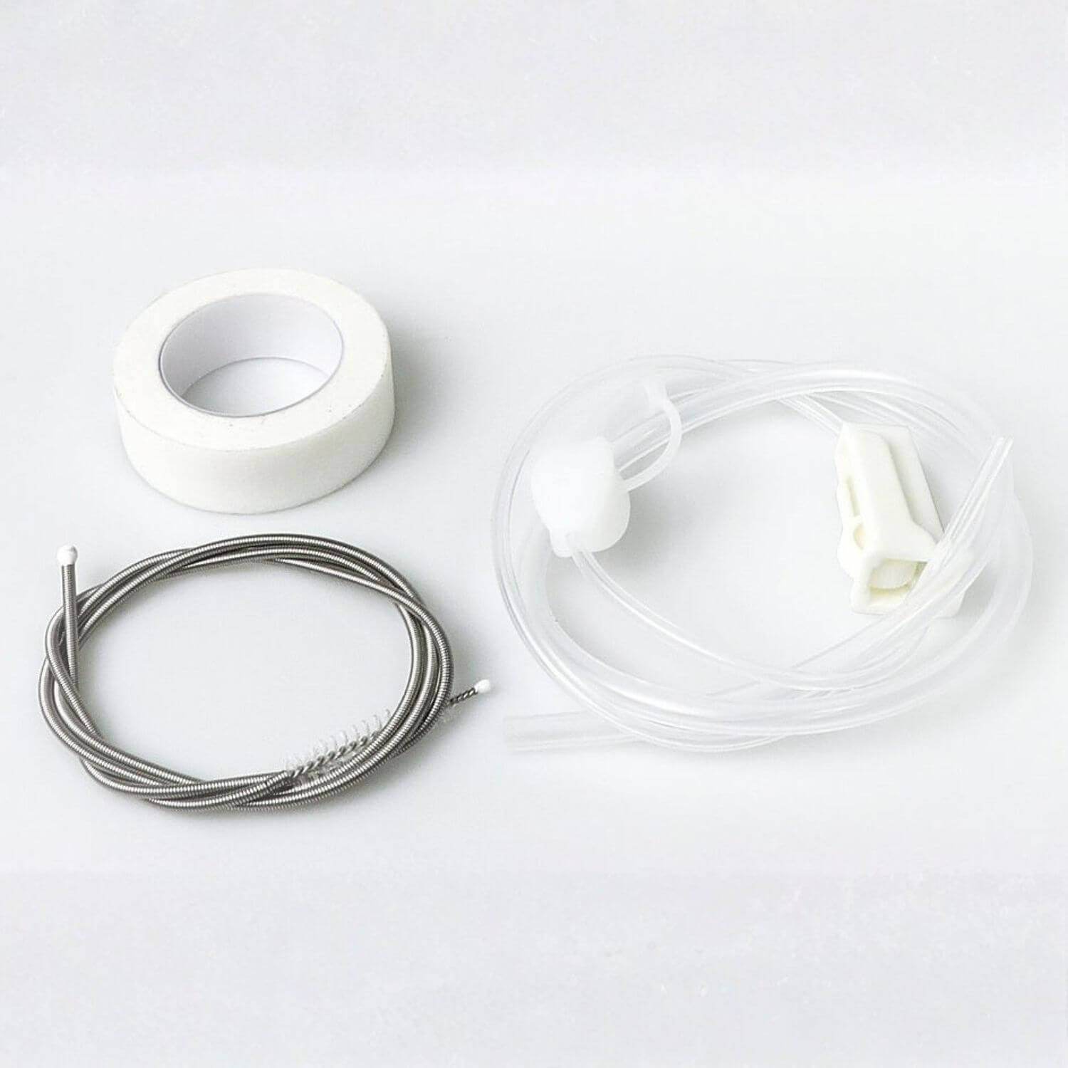 A cleaning kit containing a roll of white tape, a coiled stainless steel wire brush, and clear plastic tubing with white plastic connectors, laid out on a white background.