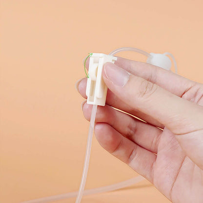 A hand holding a small white plastic tube connector with a clear tubing piece and a thin green wire, against a soft peach background.