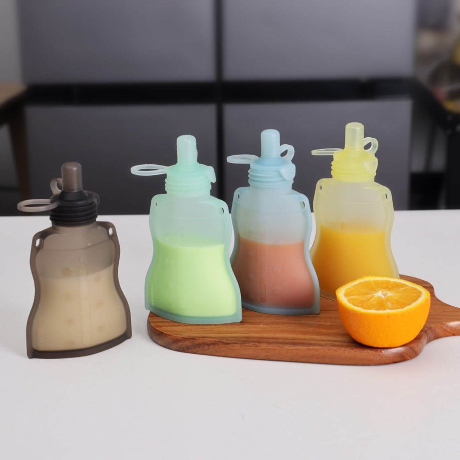 Set of Haakaa Silicone Yummy Pouches on a wooden board with an orange half.