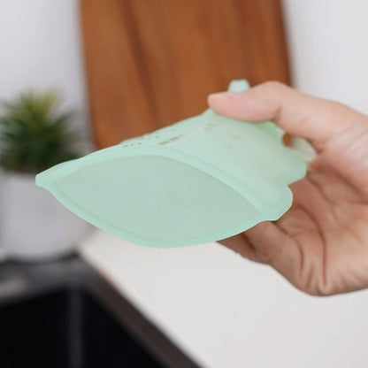 Hand holding a light green silicone pouch over a white surface with a blurred background