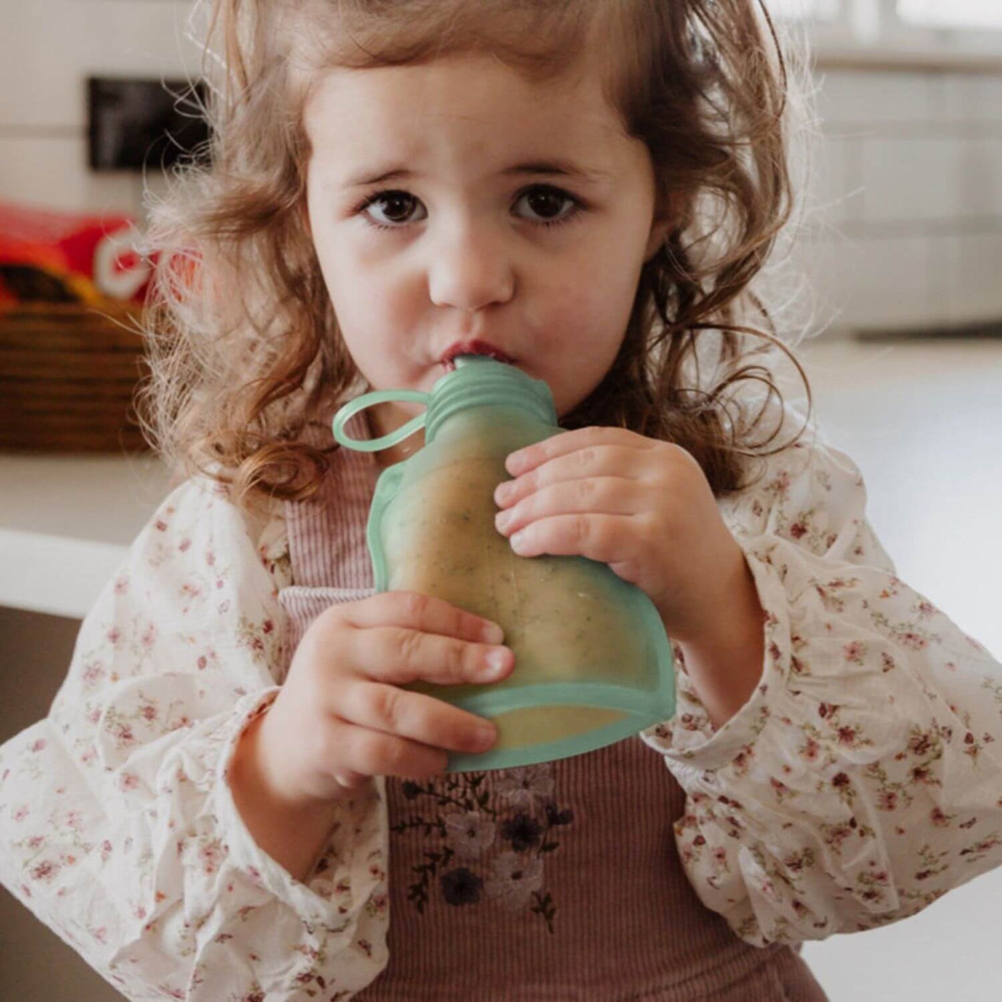 Child drinking from a Haakaa Silicone Yummy Pouch indoors