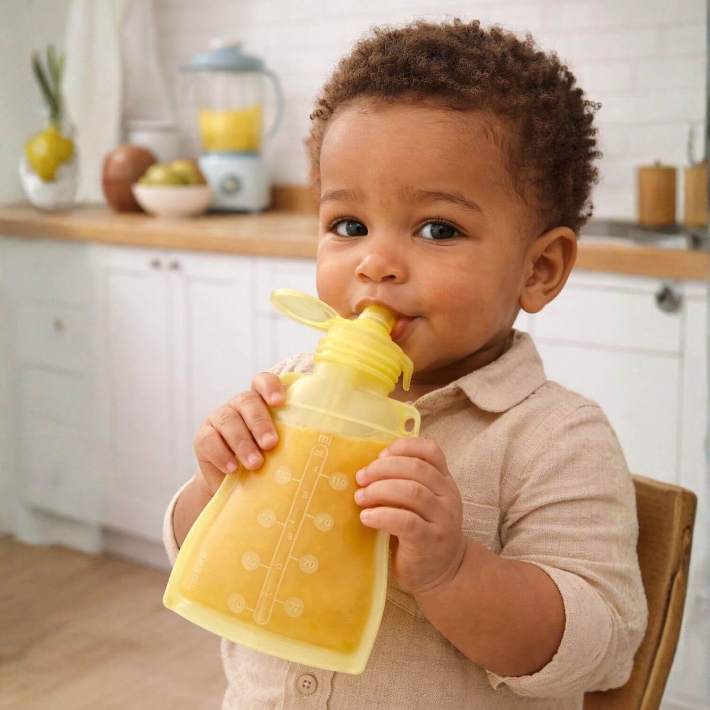 Child drinking from a yellow pouch in a kitchen setting