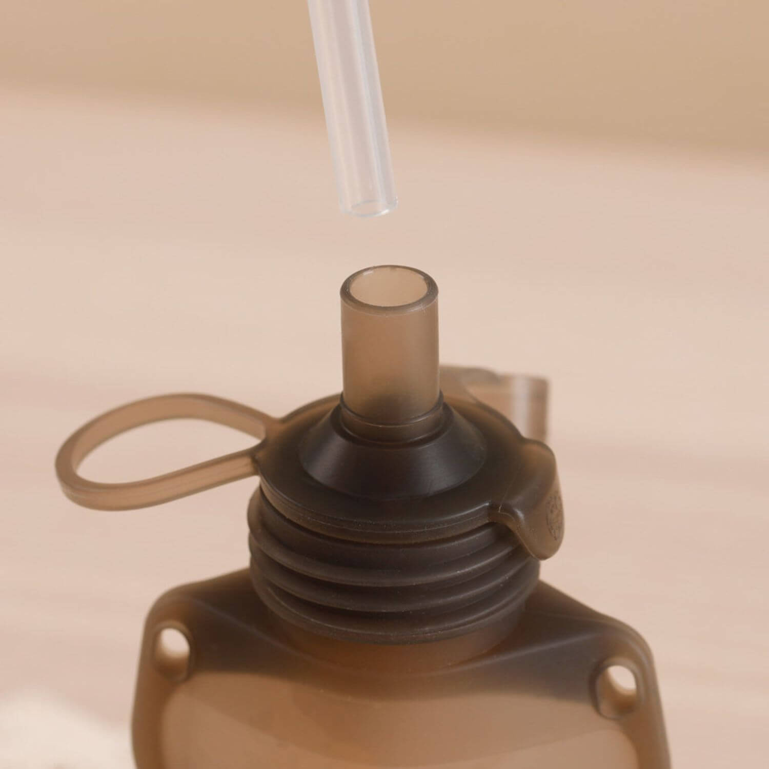 Close-up of a brown silicone pouch bottle with a straw on a beige background