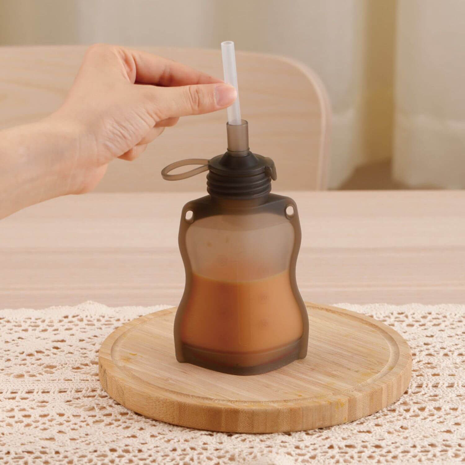 Hand holding a brown pouch with a straw on a wooden coaster.