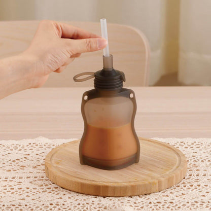 Hand holding a brown pouch with a straw on a wooden coaster.