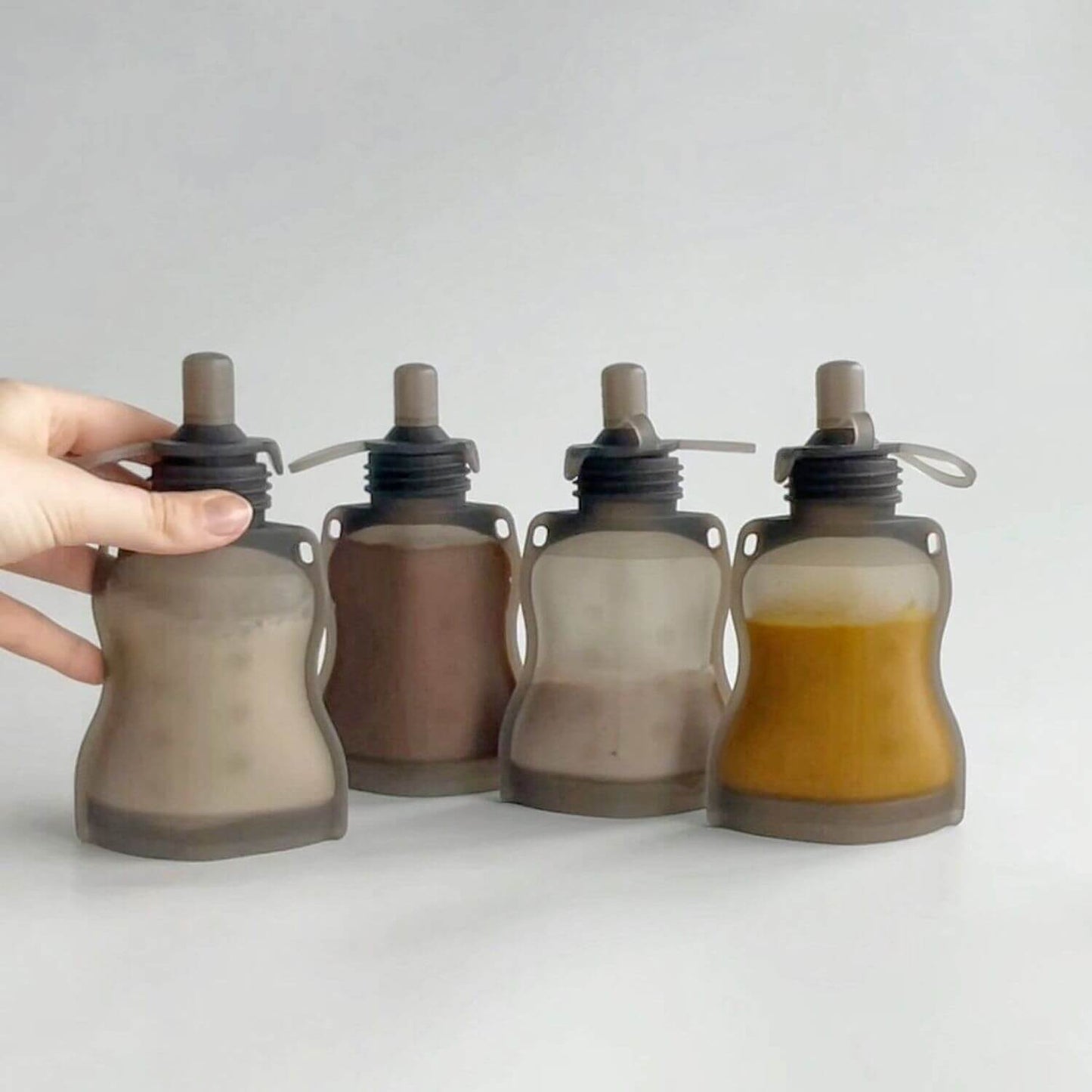 Set of four Haakaa Silicone Yummy Pouches with a hand holding one on a light gray background