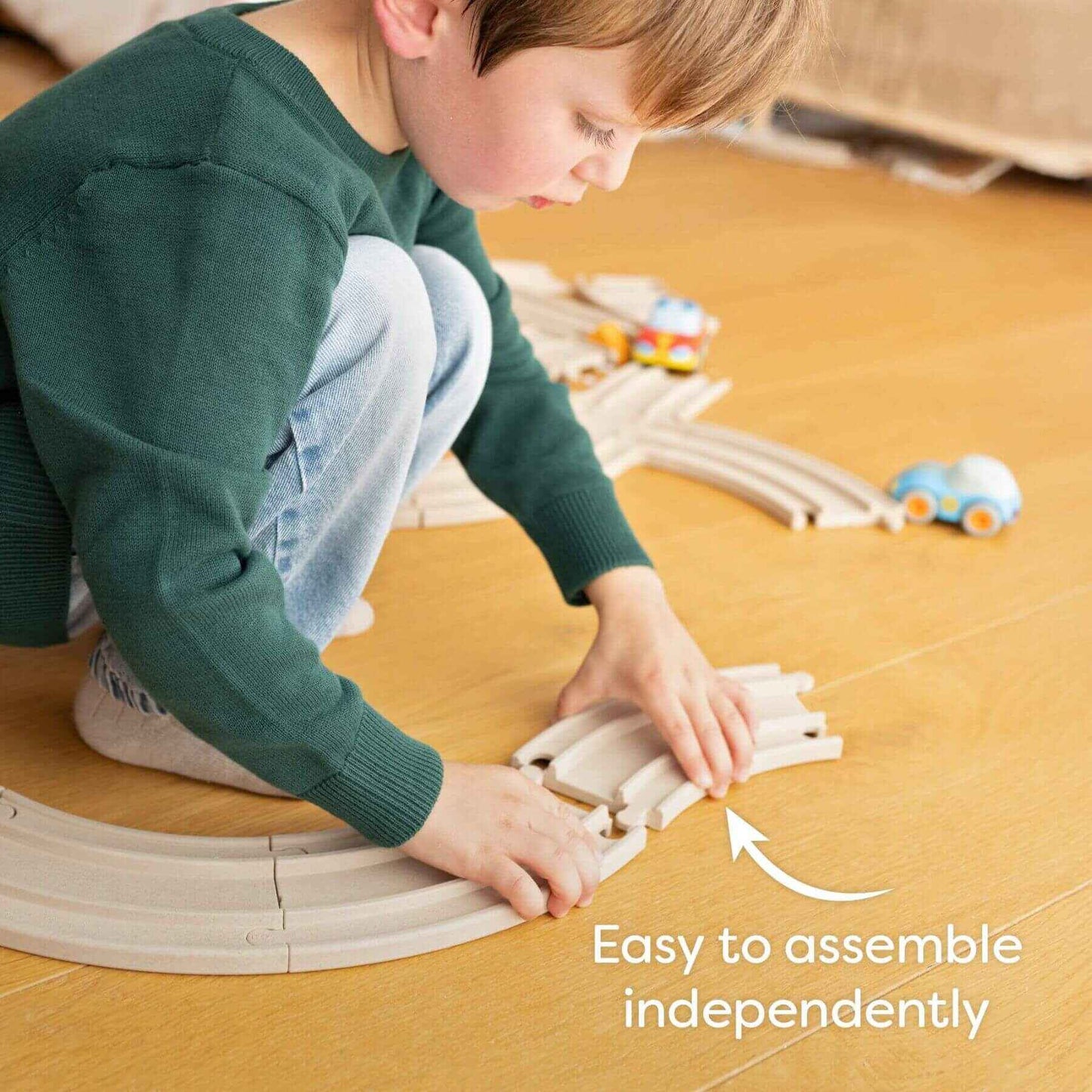 Child playing with a toy train set on a wooden floor