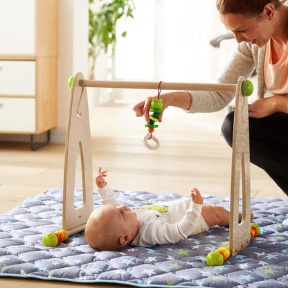 Baby playing with HABA USA Color Fun Play Gym Activity Center, with a woman assisting.