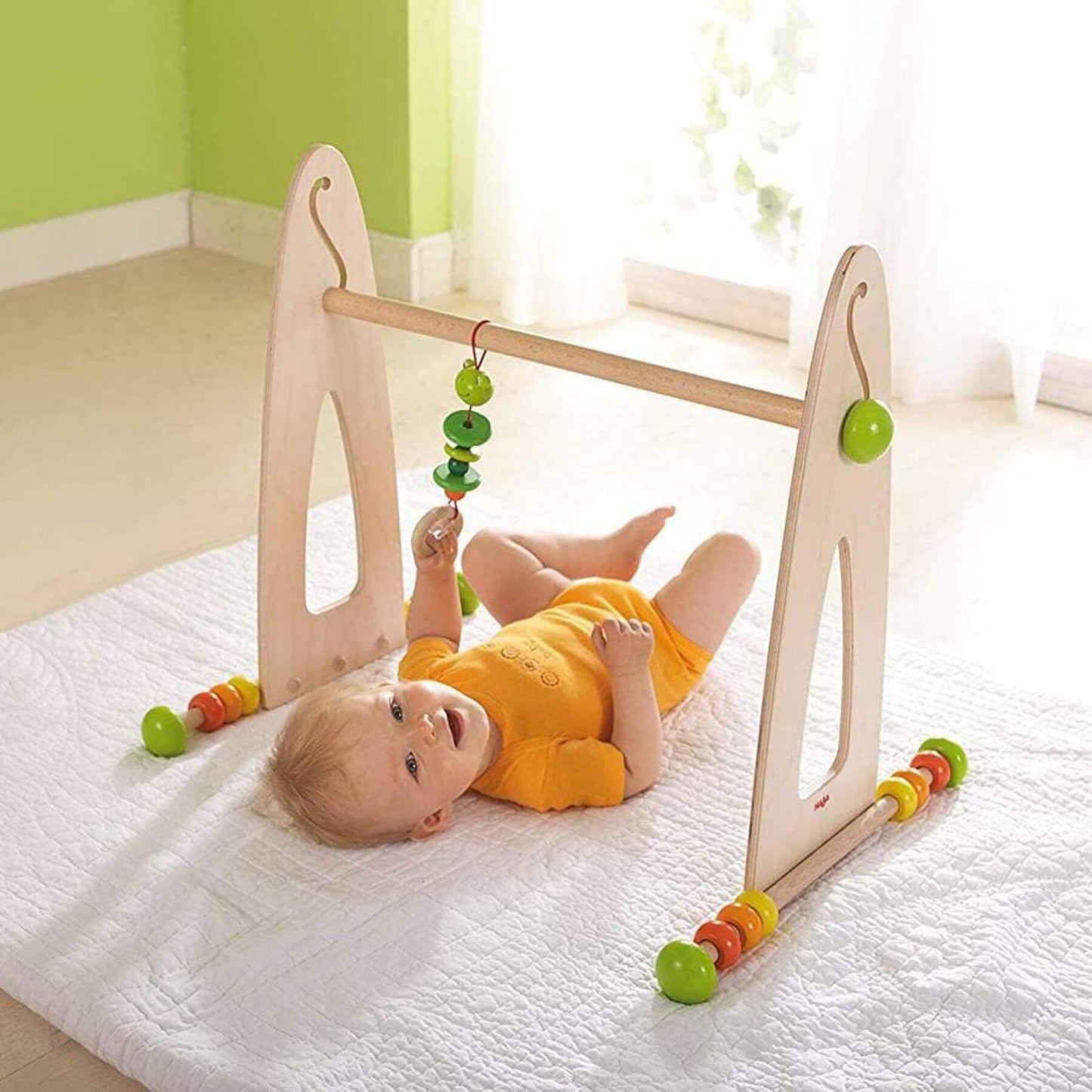 Baby playing with HABA USA Color Fun Play Gym Activity Center on a white blanket.