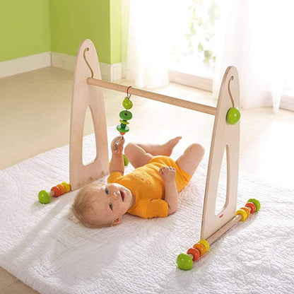 Baby playing with HABA USA Color Fun Play Gym Activity Center on a white blanket.