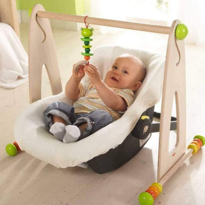 Baby playing with HABA USA Color Fun Play Gym Activity Center in a baby seat