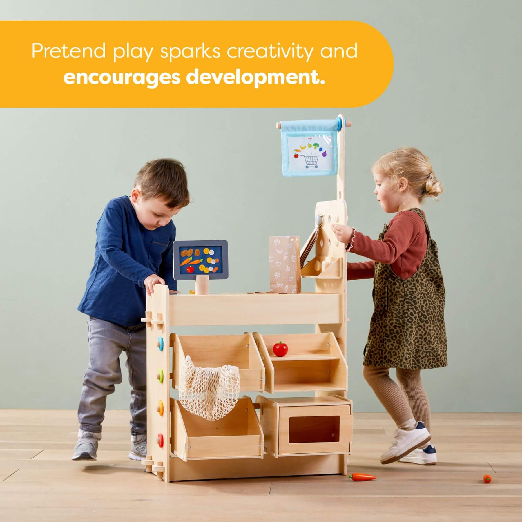 Two children playing with HABA USA Creative Play 3 in 1 – Play Kitchen, Store & Workshop in a room with a light gray wall.