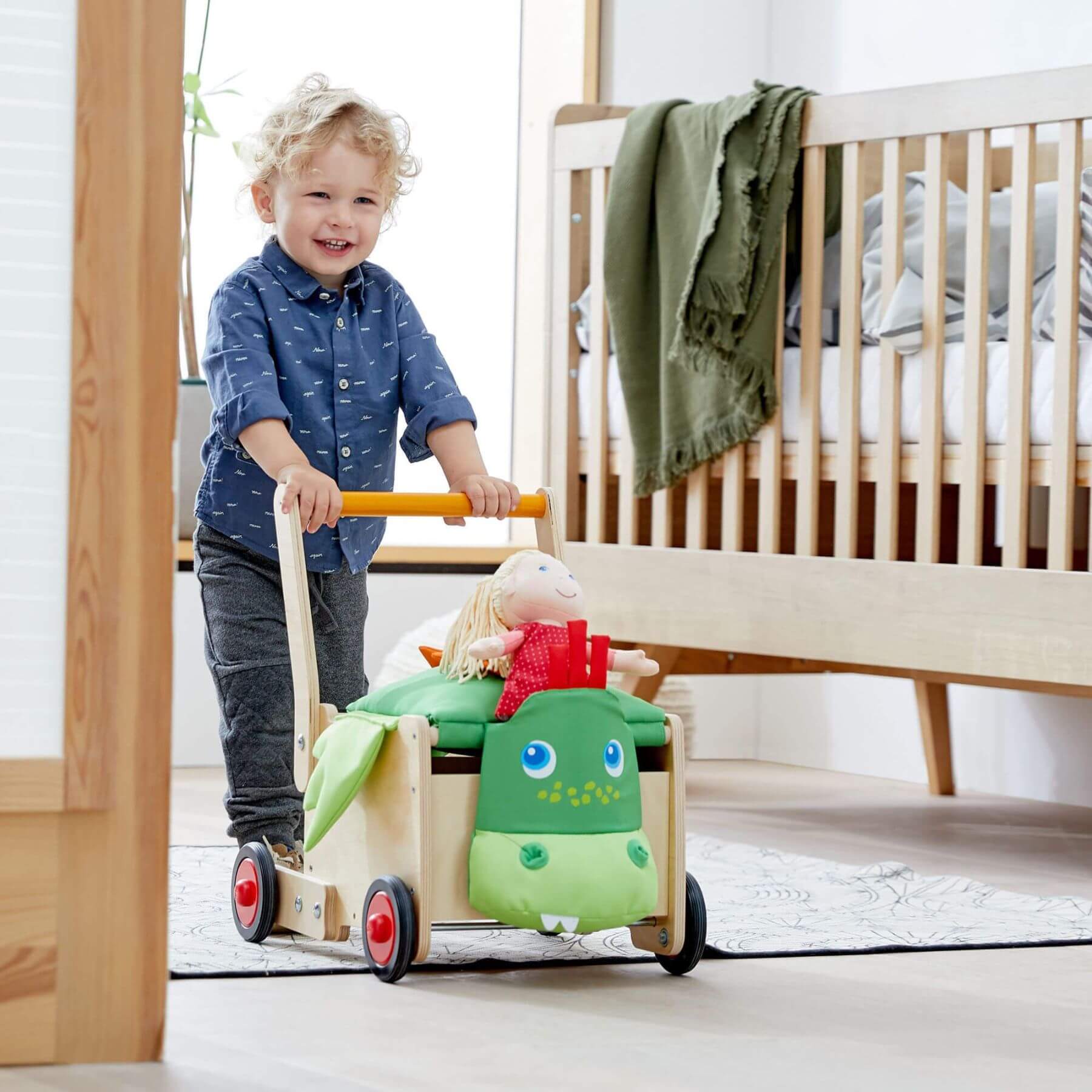 Child pushing HABA USA Dragon Wagon Baby Walker in a bedroom setting.