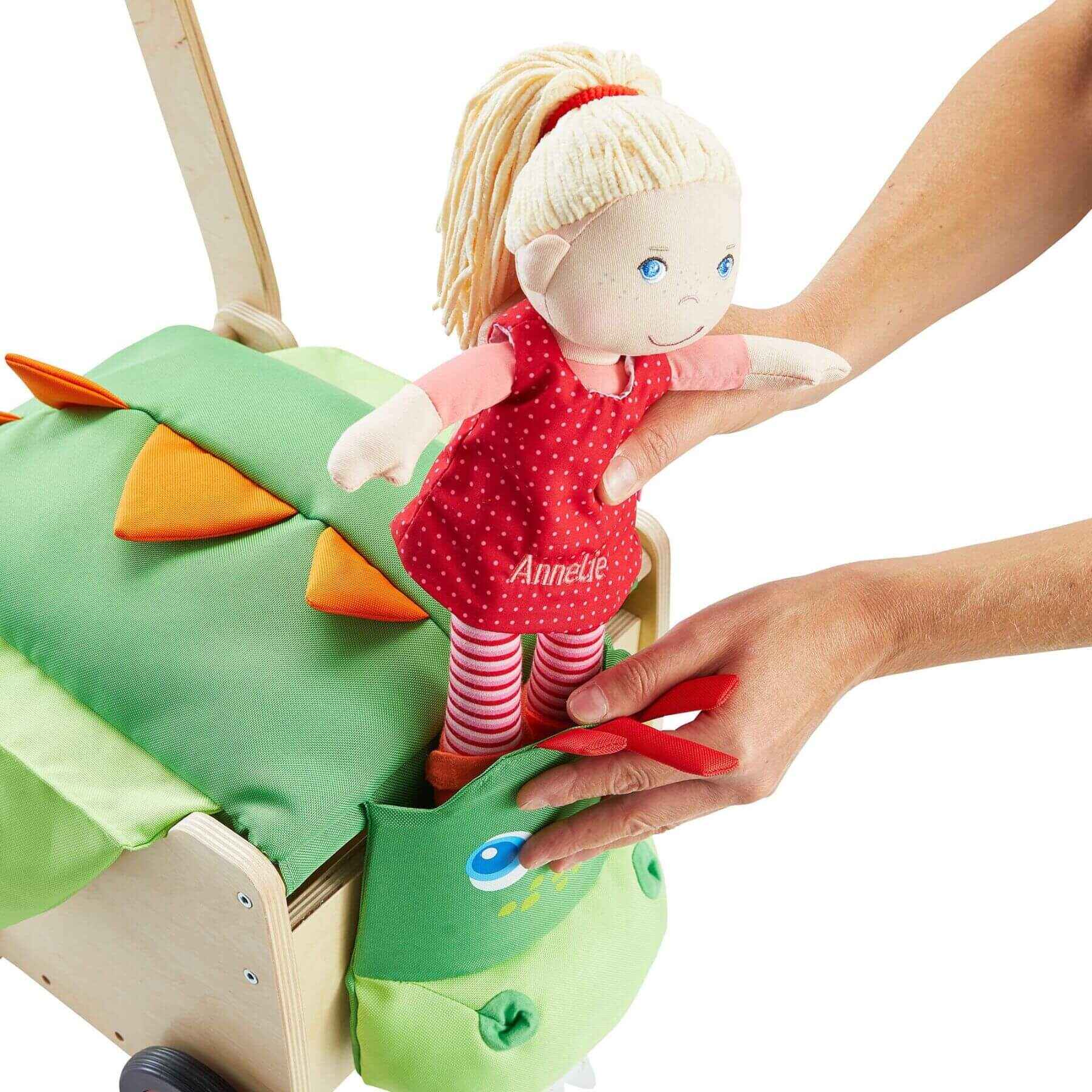 Child's hand placing a doll with blonde hair and a red dress into a green dragon-shaped toy.