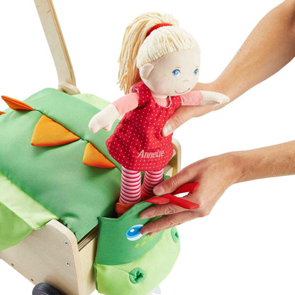 Child's hand placing a doll with blonde hair and a red dress into a green dragon-shaped toy.