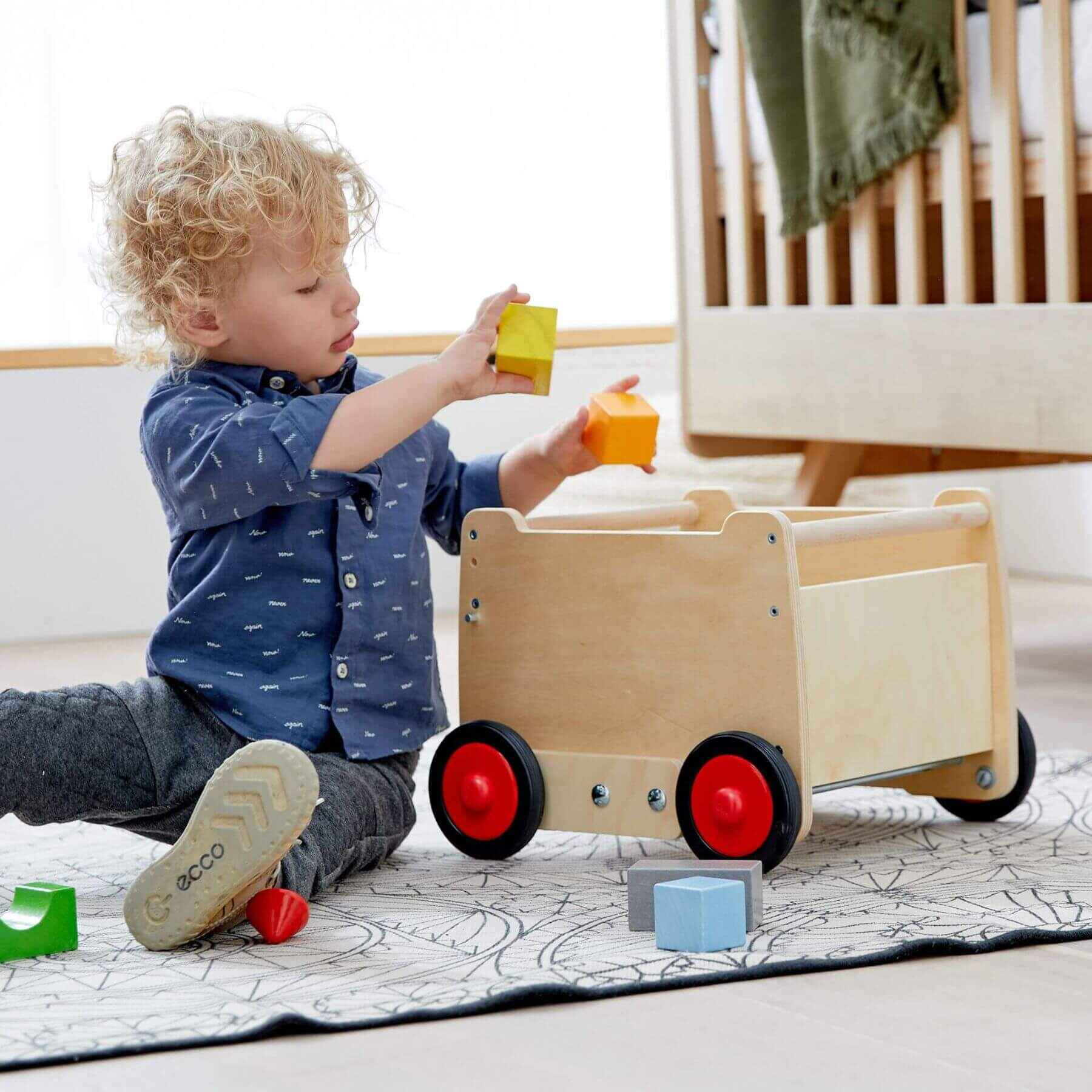 Child playing with HABA USA Dragon Wagon Baby Walker on a light-colored floor.