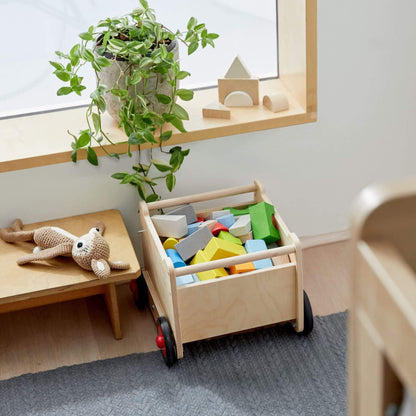 Wooden toy cart with colorful blocks in a room with a shelf and plant