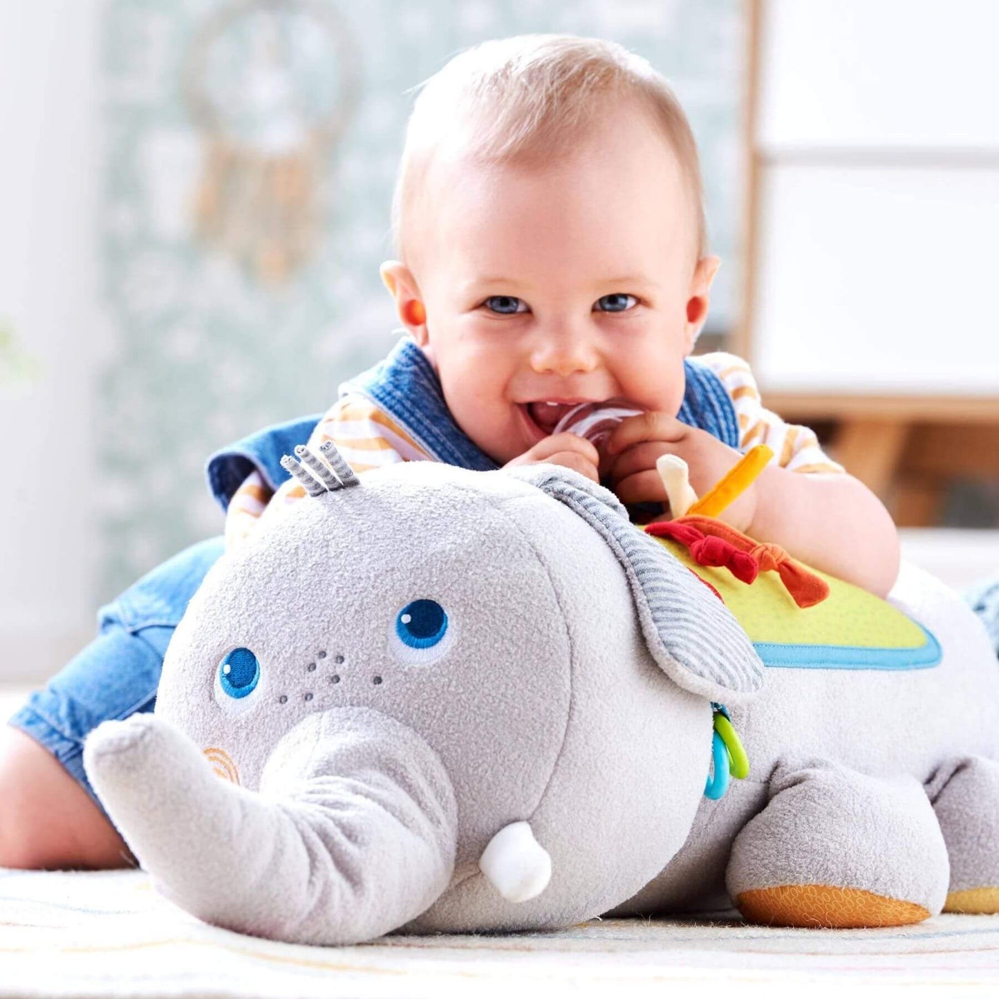 Baby holding HABA USA Elephant Discovery Pillow in a room with a blurred background