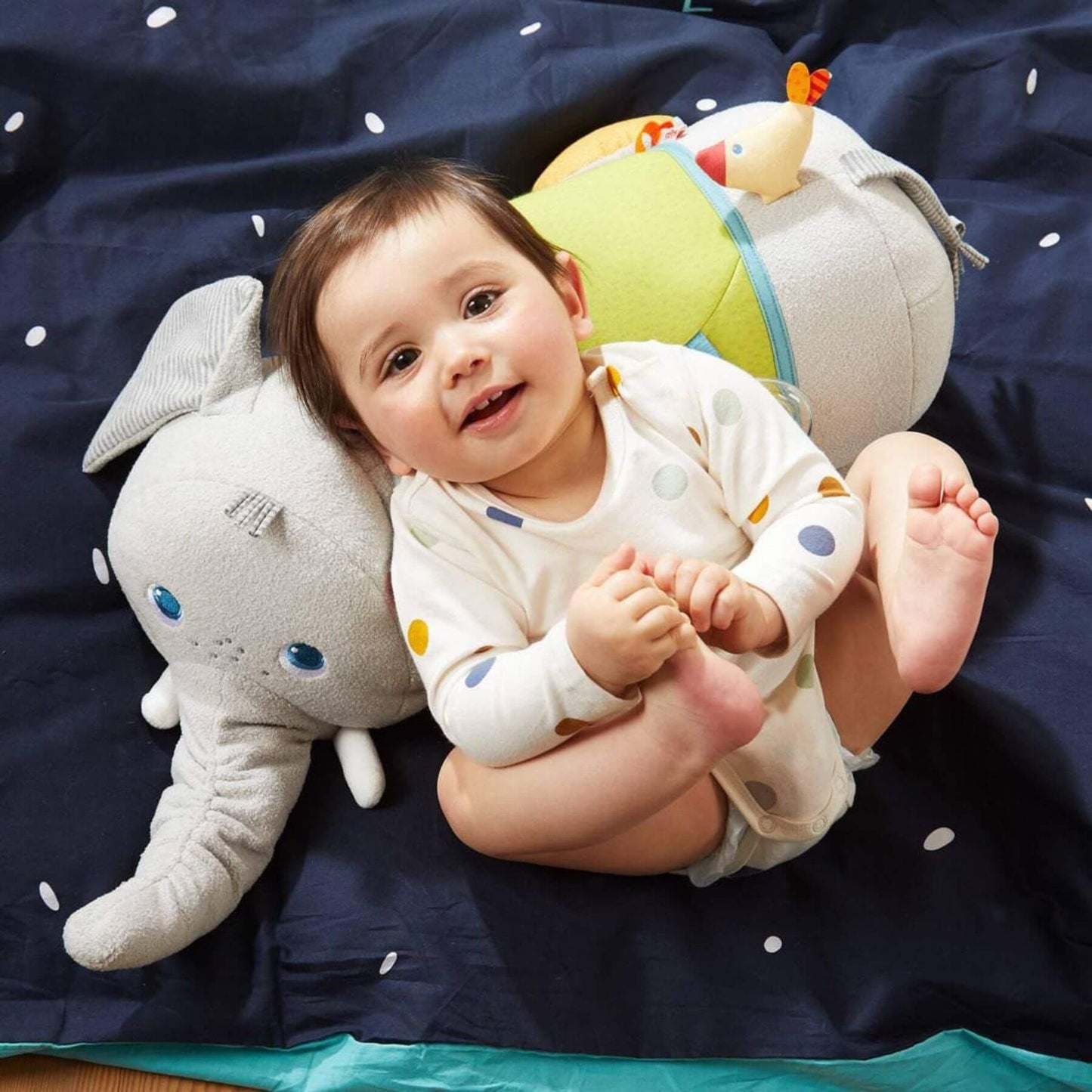 Baby lying on a dark blue blanket with HABA USA Elephant Discovery Pillow