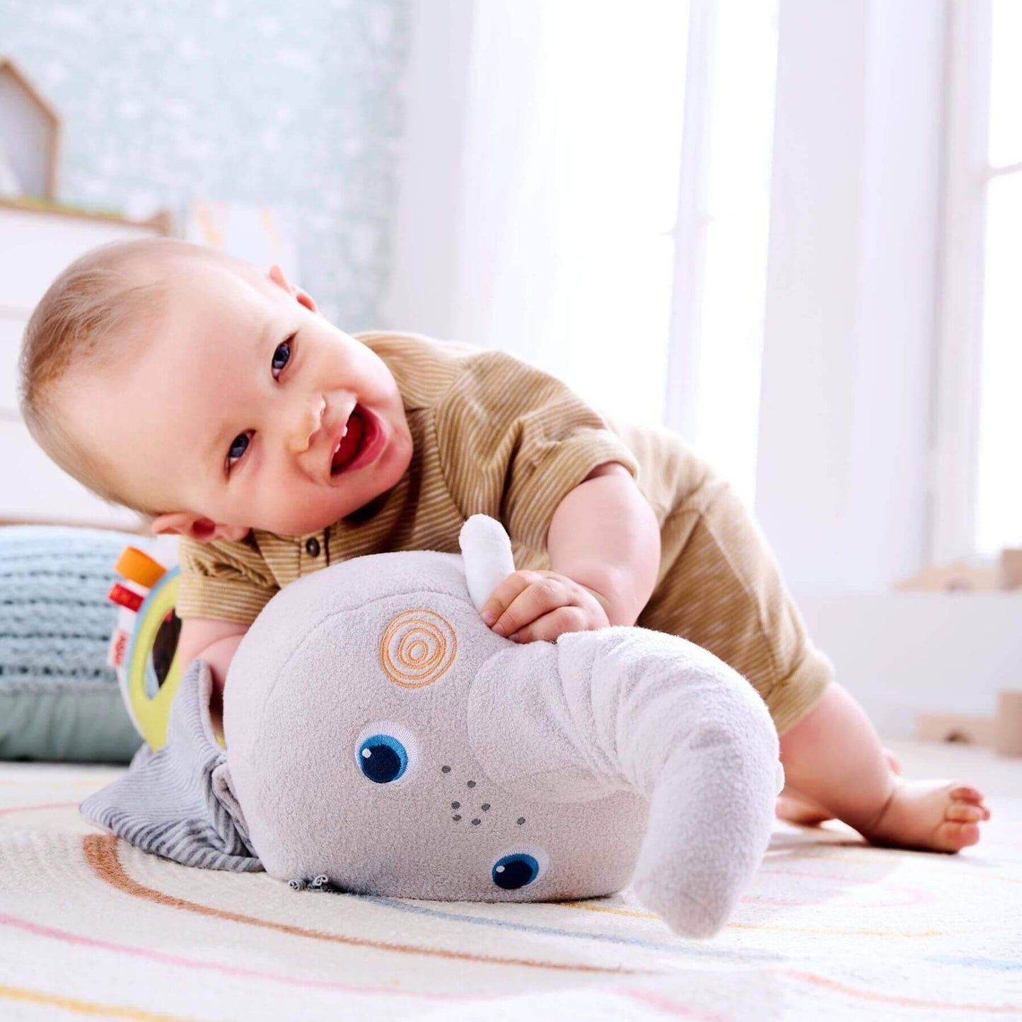 Baby playing with HABA USA Elephant Discovery Pillow on a bed in a bright room