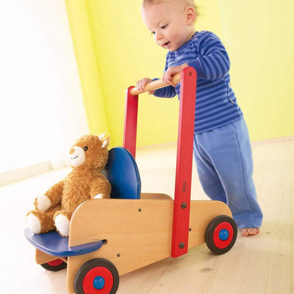 Child playing with HABA USA Walker Wagon Push Toy against a yellow wall.