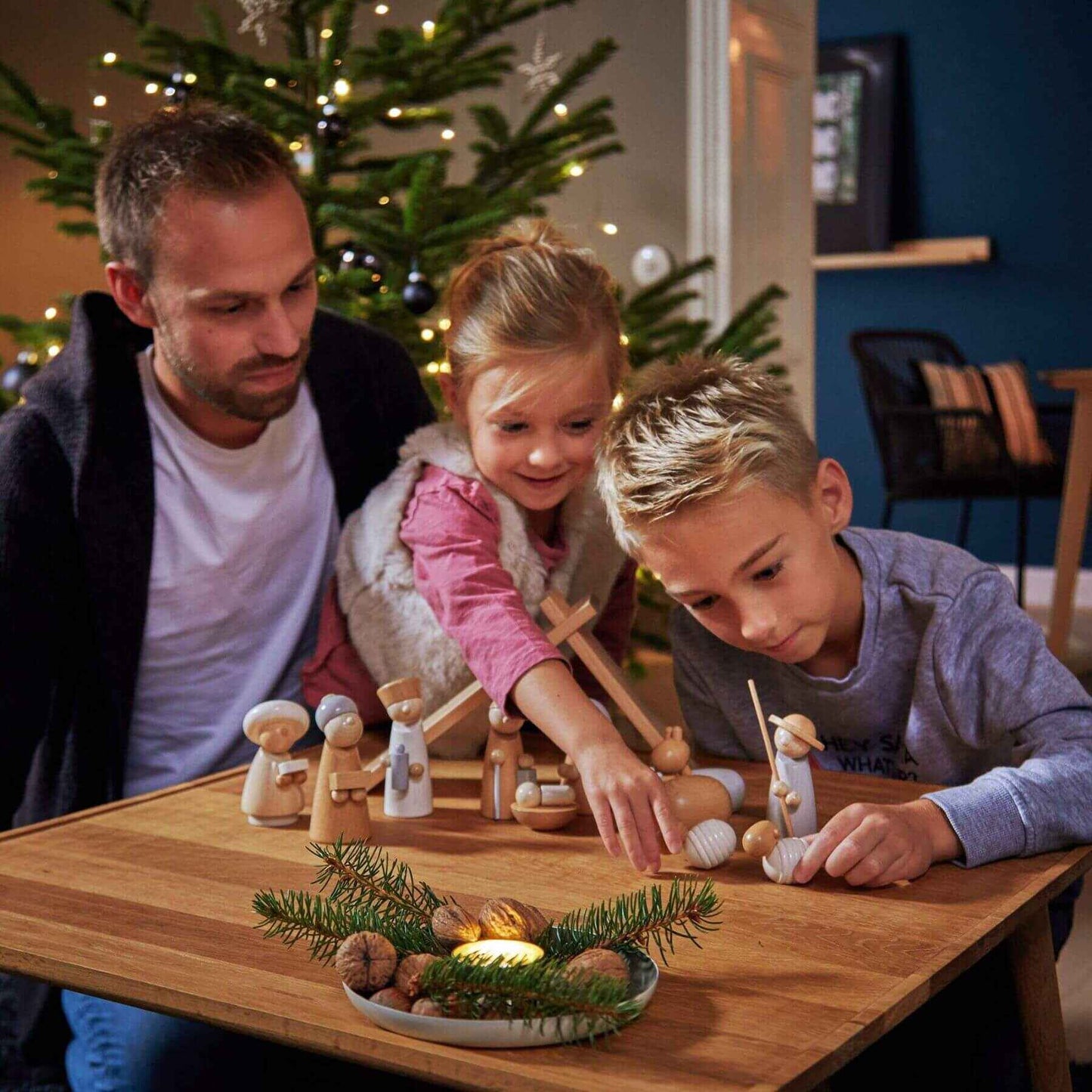 Family playing with HABA USA Natural Wood Nativity Set on a wooden table in a home setting.