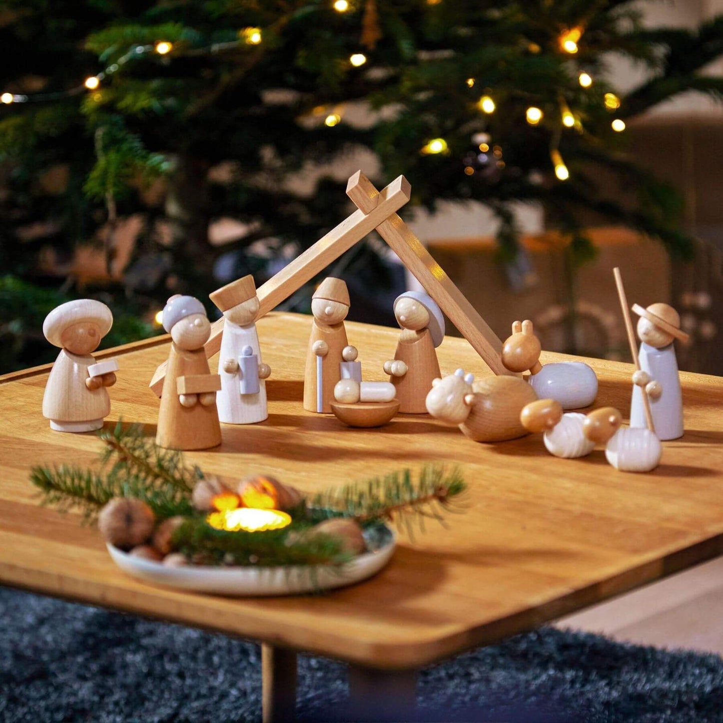 HABA USA Natural Wood Nativity Set on a table with a Christmas tree in the background