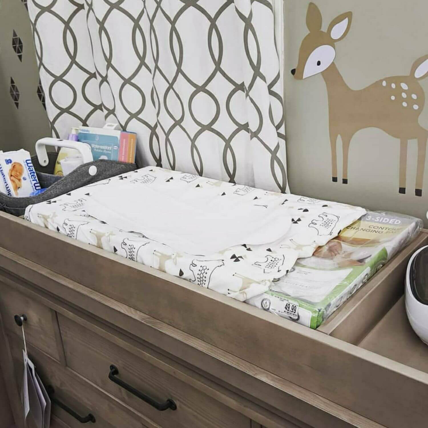 Nursery changing table with baby items and a deer wall decal.