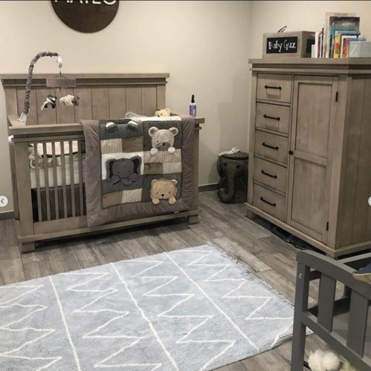 Nursery room with wooden crib, dresser, and rug featuring geometric patterns.
