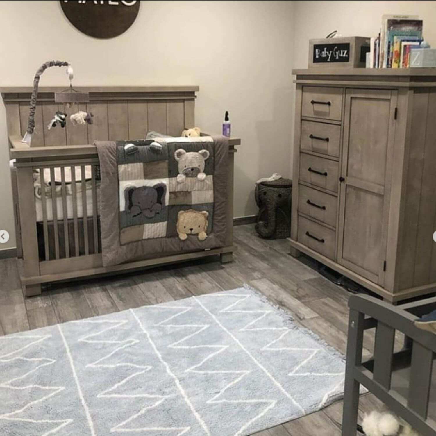 Nursery room with wooden crib, dresser, and rug featuring geometric patterns.