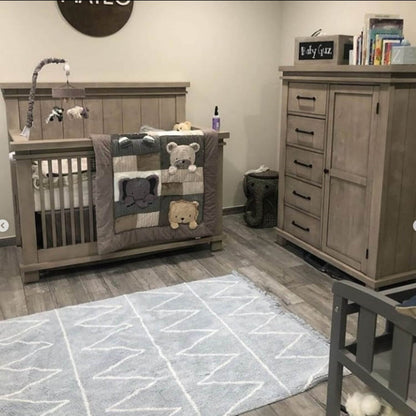 Nursery room with wooden crib, dresser, and rug featuring geometric patterns.