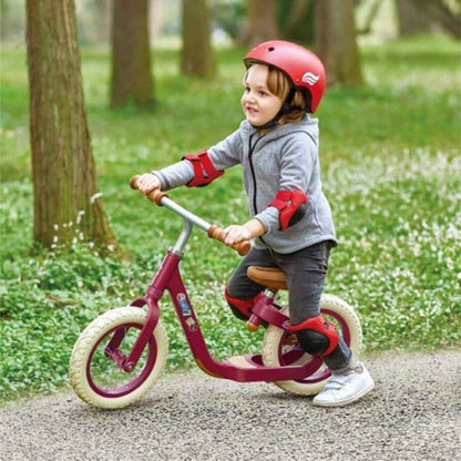 Child riding Hape Learn to Ride Balance Bike Red with safety gear in a park setting