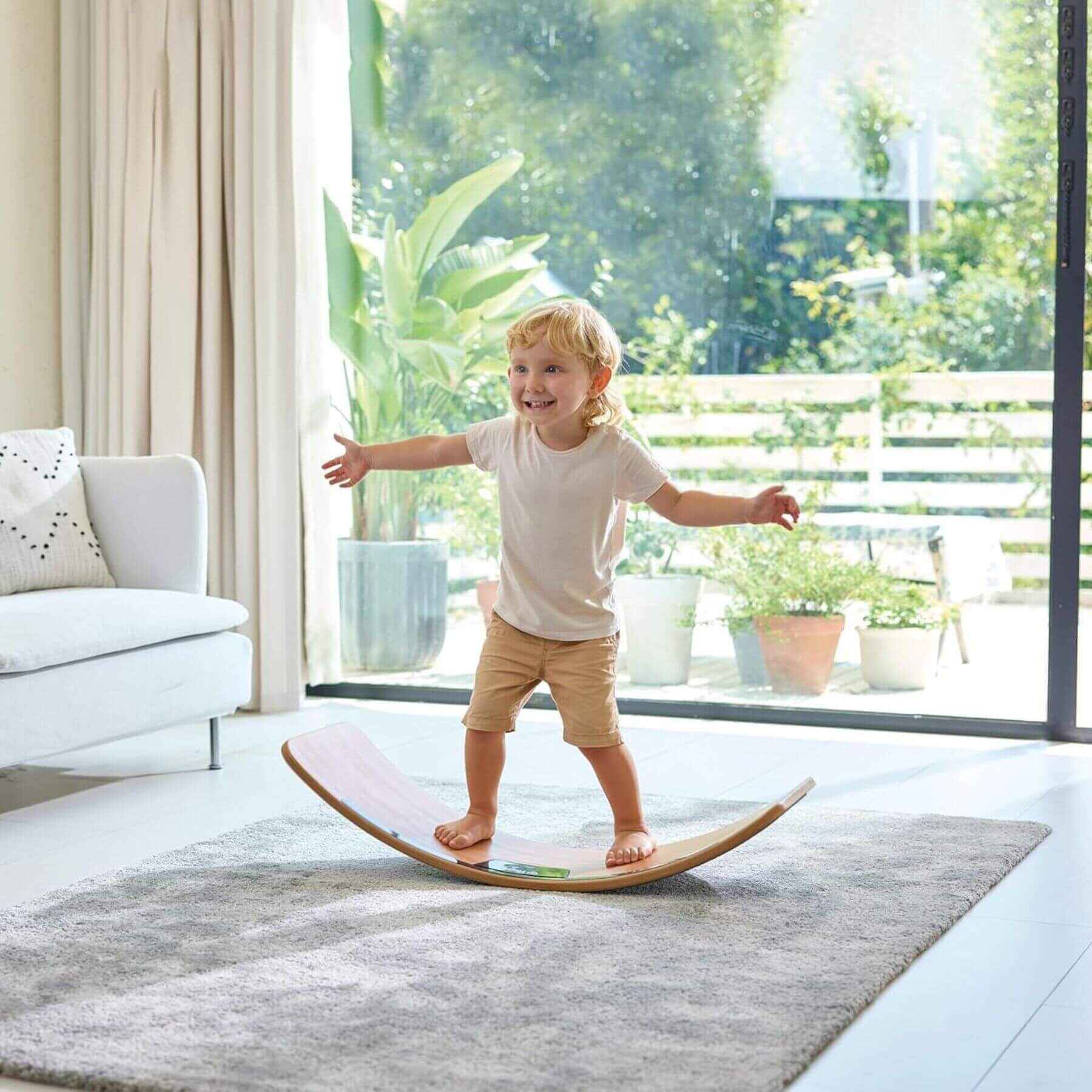 Child balancing on Hape Light Up Balance Board in a modern living room with large windows.