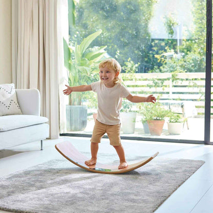 Child balancing on Hape Light Up Balance Board in a modern living room with large windows.