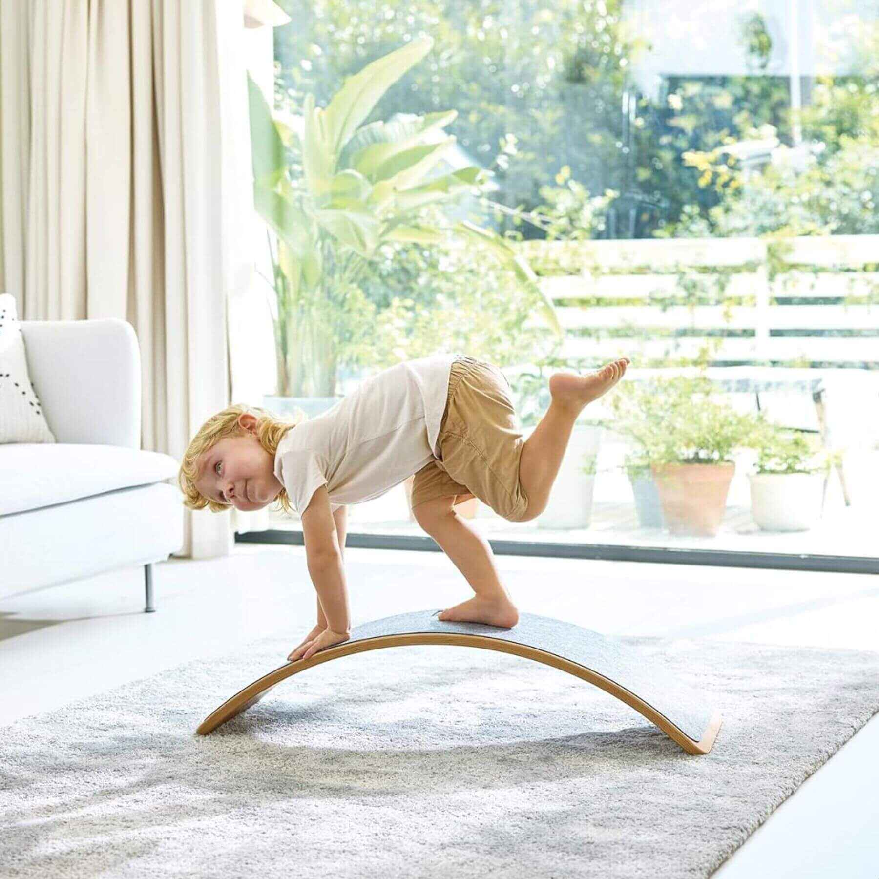 Child balancing on Hape Light Up Balance Board in a bright living room with large windows.
