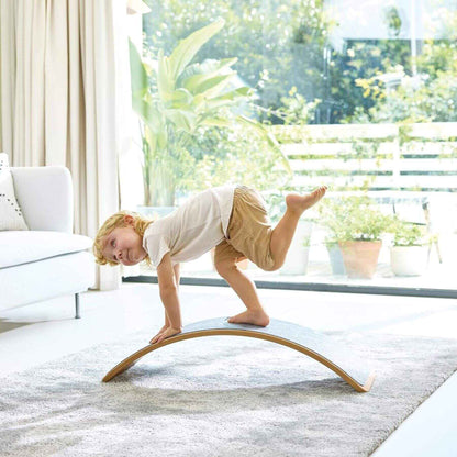Child balancing on Hape Light Up Balance Board in a bright living room with large windows.