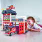Child playing with Hape City Fire Station on a wooden floor.
