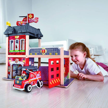 Child playing with Hape City Fire Station on a wooden floor.