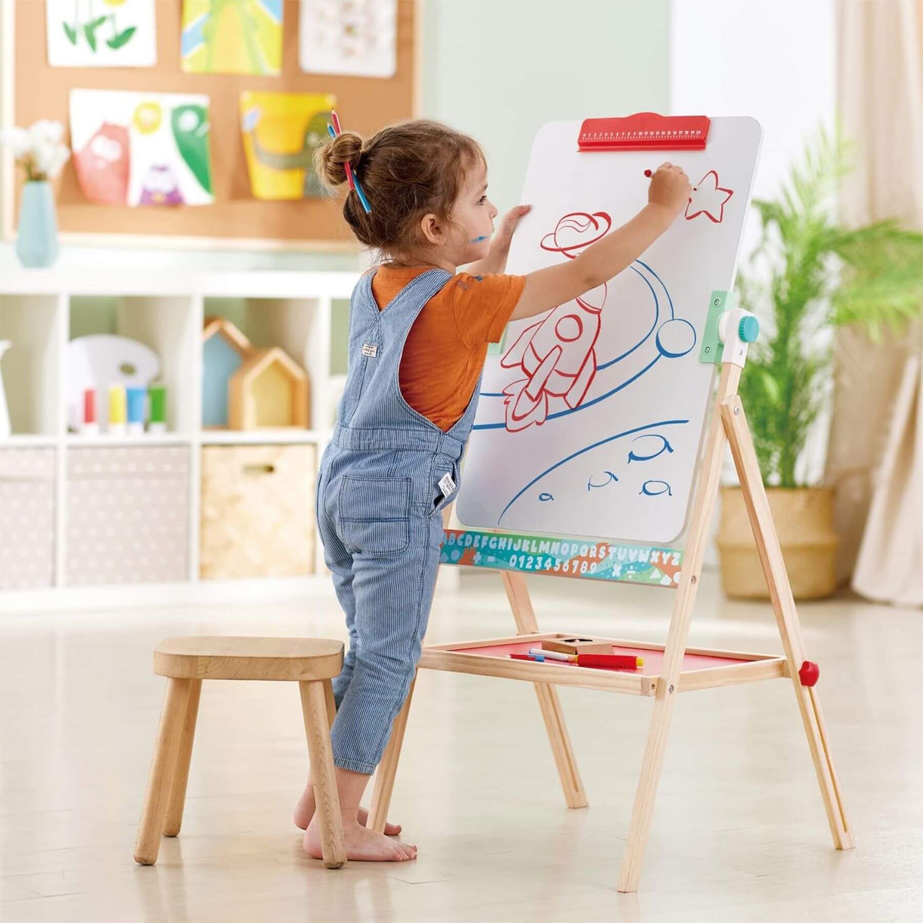 Child drawing on Hape Flip Flat Easel with colorful markers in a bright room.