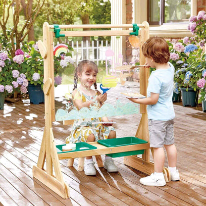 Two children playing with Hape Outdoor Art Easel outdoors on a wooden deck.