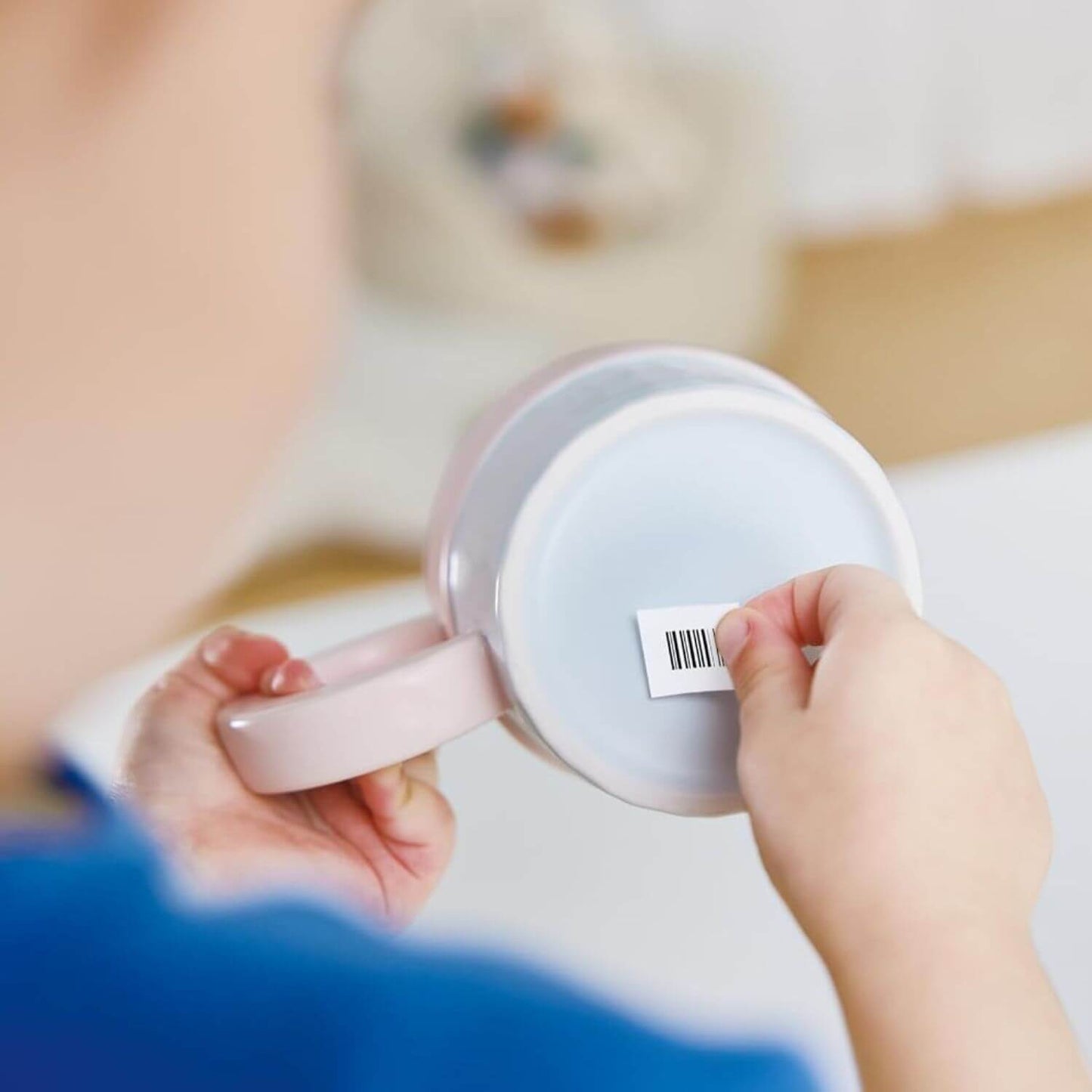 Person holding a white electronic device with a label, blurred background