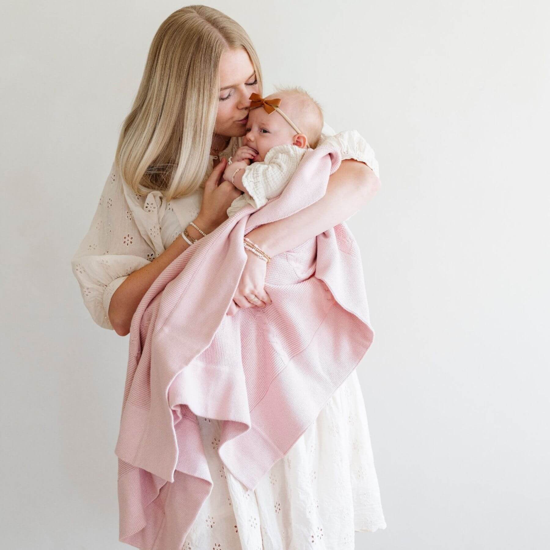Woman holding a baby wrapped in Saranoni Heirloom Cotton Knit Receiving Blanket against a white background