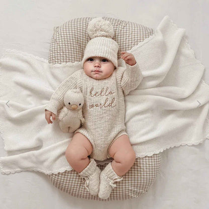 Baby in Newborn Hello World Knitted Bodysuit Set, lying on a checkered cushion with a white blanket.