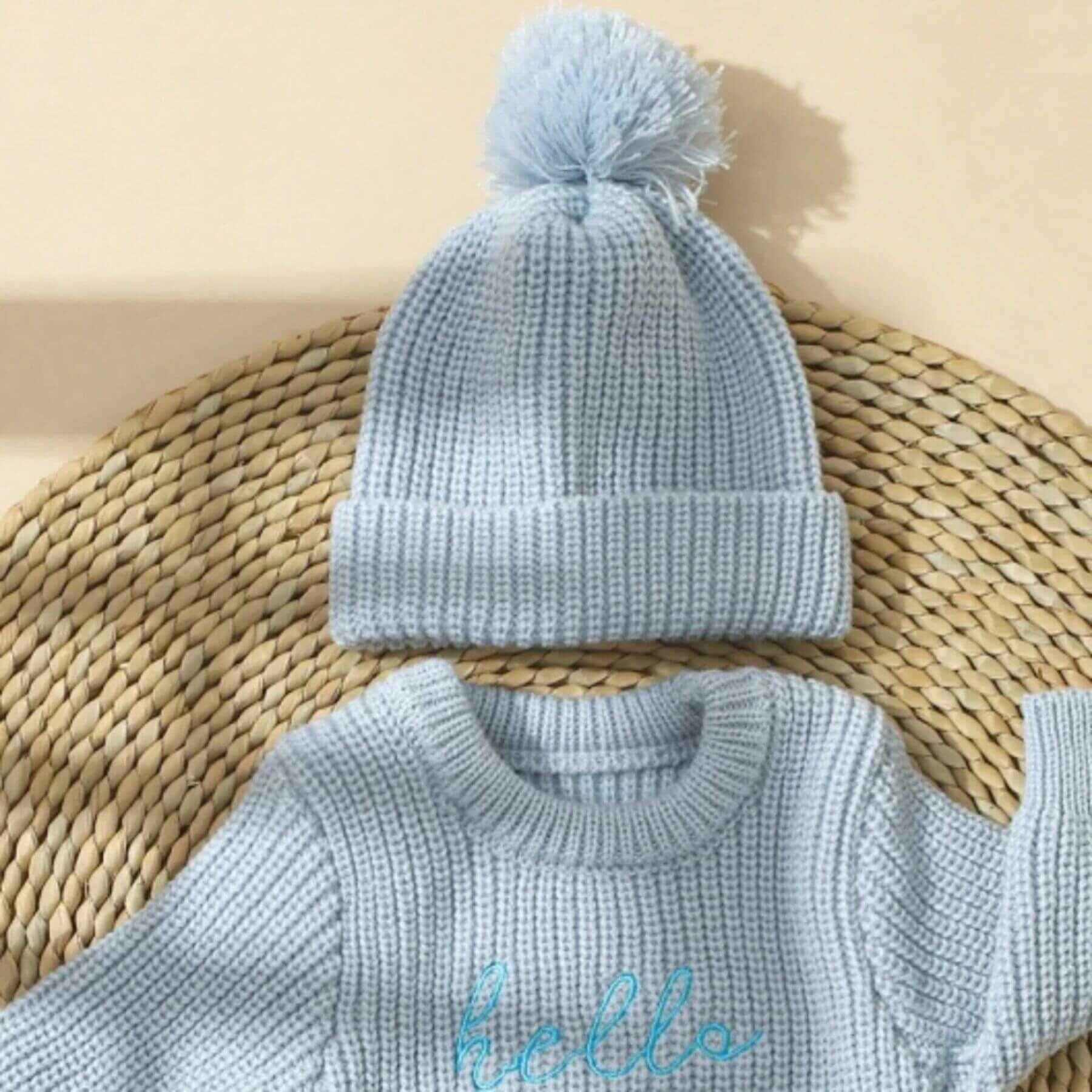 Newborn Hello World Knitted Bodysuit Set Blue on a woven mat.