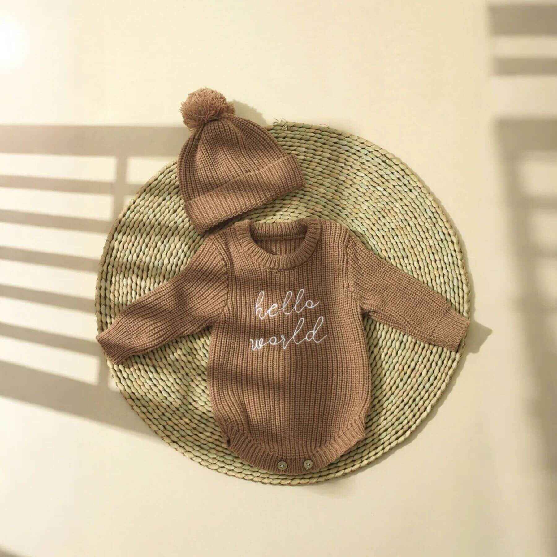 Newborn Hello World Knitted Bodysuit Set Brown on a woven mat.