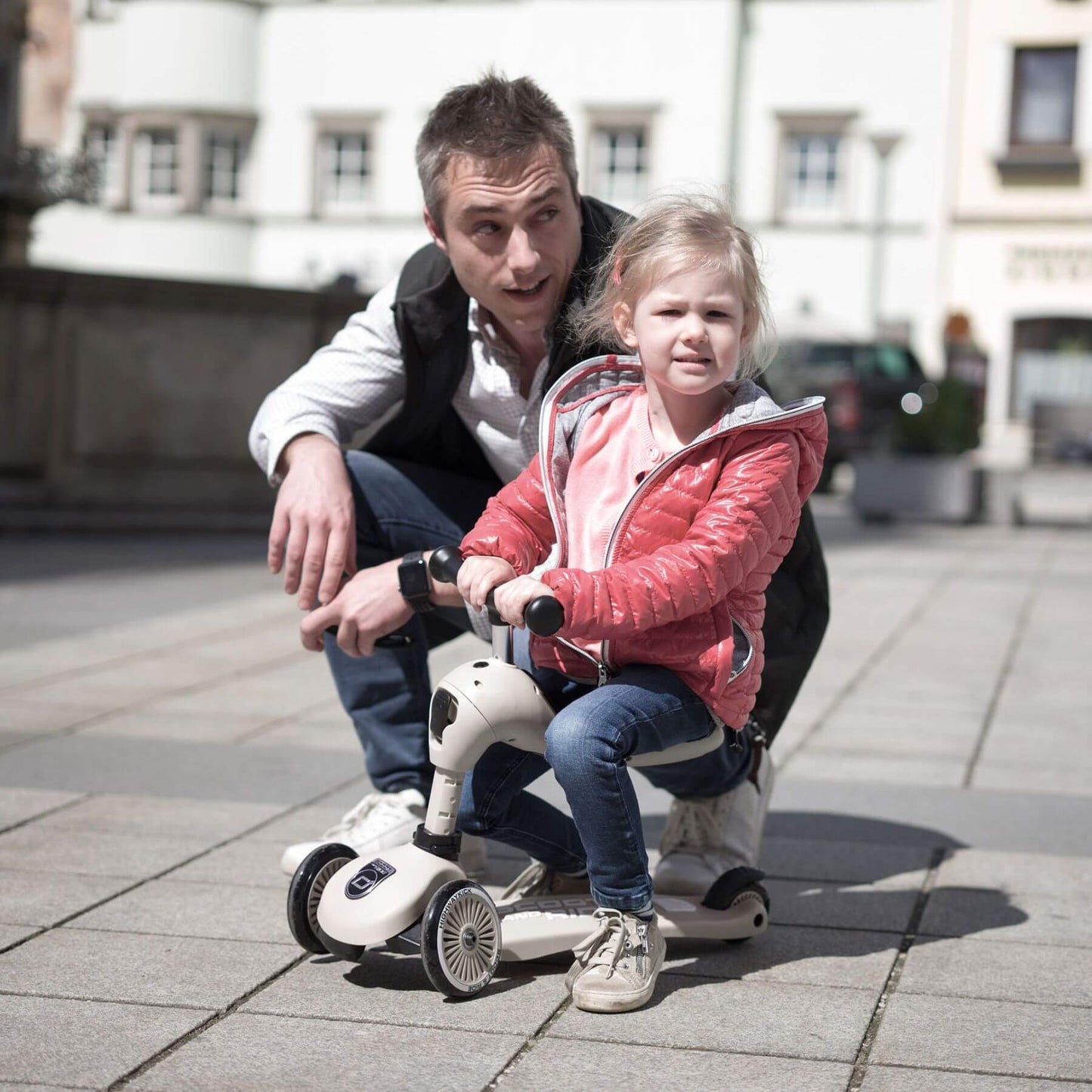 Man and young girl riding a scooter together on a city street.