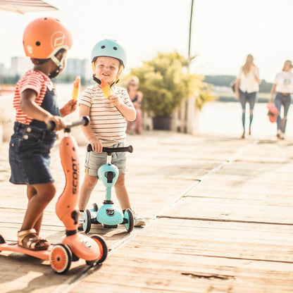 Two children on scooters with helmets at a waterfront