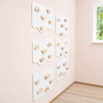 Wooden climbing wall panels on a light pink wall with a window showing greenery.